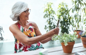 a smiling happy and healthy older woman grey and proud taking pictures among her many houseplants