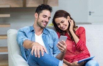 a smiling young couple on a sofa looking at a mobile phone