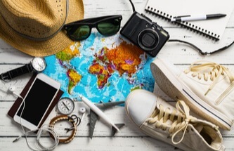 map of the world with travel paraphenalia around - sunglasses, sport shoes, compass, glasses, camera