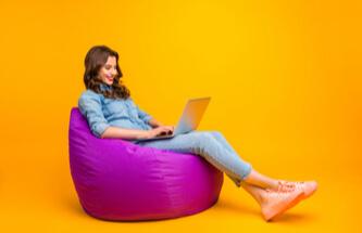 woman playing Everygame Casino games on her laptop while sitting on a purple bean bag chair in a yellow room