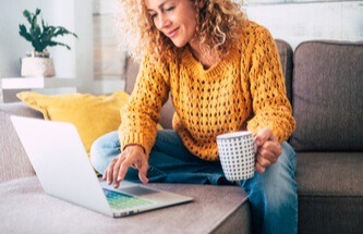 pretty millennial woman with curly golden hair enjoying online casino gaming on her sofa with a cup of coffee in her hand