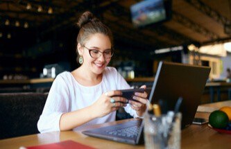 woman taking a break from her work on laptop to play a game on her phone.