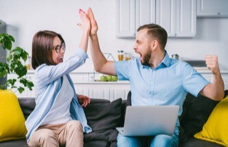 couple sitting on the sofa doing a high 5 after winning at Everygame Casino blackjack on their laptop