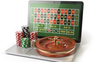 roulette wheel and chips sitting on an open laptop with a roulette betting table on the screen
