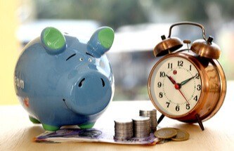 a blue piggy bank with money on the table and an alarm clock showing time and money managem