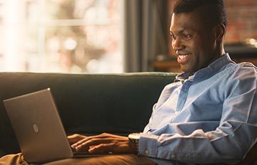 young man happily playing casino games on his laptop while sitting comfortably on his sofa