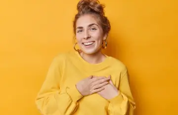 a young woman holding her hands at her heart as she looks at the camera showing a deep sense of appreciation