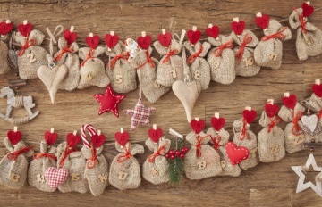 Little Advent calendar hessian gift bags with dated red heart pegs attaching them to string on a wooden table