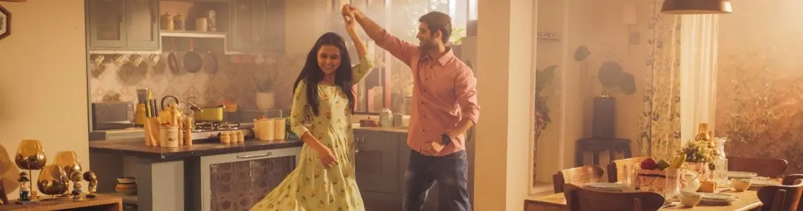 a young couple dancing in the kitchen with big smiles on their faces