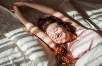 a young woman waking up happily from a good night's sleep