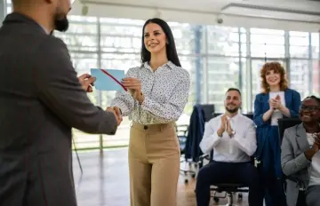 an employee receiving a bonus from their employer or department leader while colleagues applaud in the background