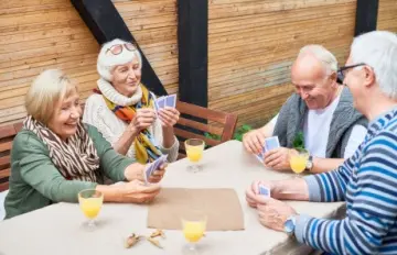 Two happy and smiling senior citizen couples enjoying a card game together.