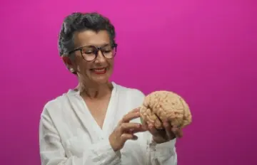 an older female with grey hair either a lab researcher or a doctor holding a brain and expressing deep curiosity over it