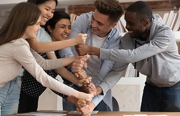 five smiling and happy young adults playing a game in which they create a vertical line by placing fists one on top of the other