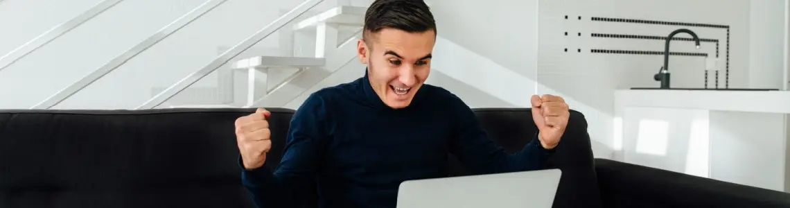 Happy man playing casino games on his laptop and on the sofa