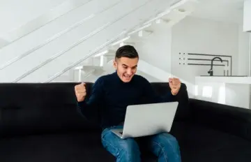 Happy man playing casino games on his laptop and on the sofa