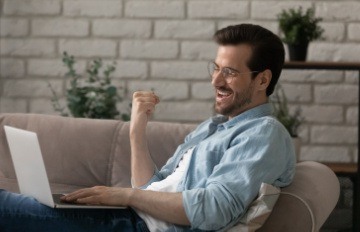 young man with short cropped beard comfortable on the sofa fist pumping a win at an online casino