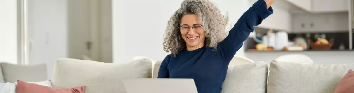 a very ecstatic middle-aged woman on her sofa with her laptop happy about an Everygame Casino win