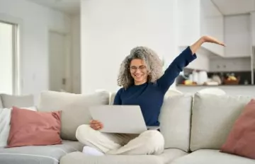 a very ecstatic middle-aged woman on her sofa with her laptop happy about an Everygame Casino win