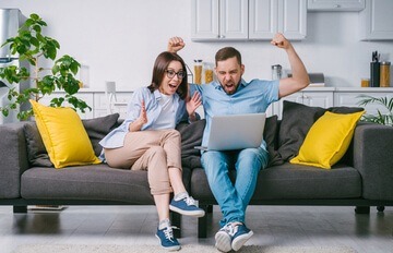 a young couple enjoying online casino gaming while sitting comfortably on their sofa at home