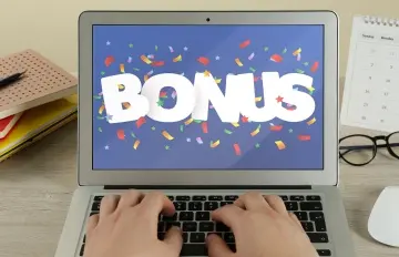 a person at their laptop with the word "BONUS" on the screen and colorful confetti all around on the screen