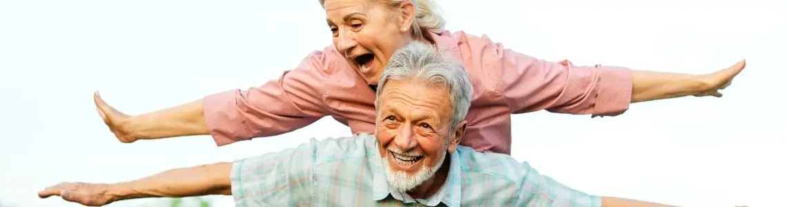 older couple having unbridled fun together as she rides on his back and both have their arms outstretched