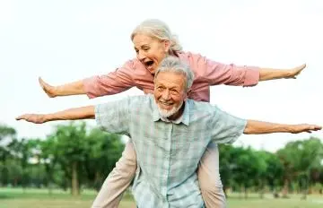 older couple having unbridled fun together as she rides on his back and both have their arms outstretched