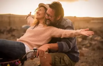 a young couple out in the middle of nowhere having fun with the woman on the handlebars of a bicycle