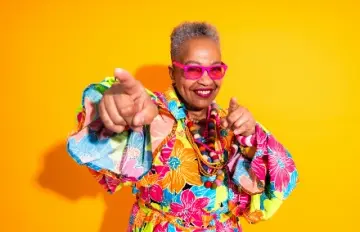 an older African American woman with salt and pepper hair, pink glasses, a dress of many colors with a big smile on her face