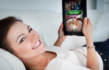 attractive professional woman on her sofa playing at an online casino on her tablet. she has a big smile on her face.