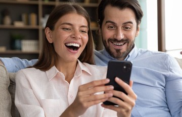 young couple enjoying online casino games from the comfort of their sofa.  they are both smiling broadly.