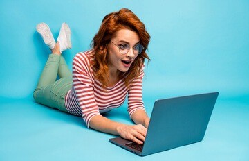 young woman lying on the floor having fun playing Everygame Casino games on her laptop