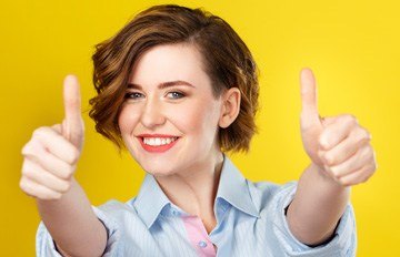 a young woman with a big smile looking directly into the camera and showing two thumbs up as a sign of PMA