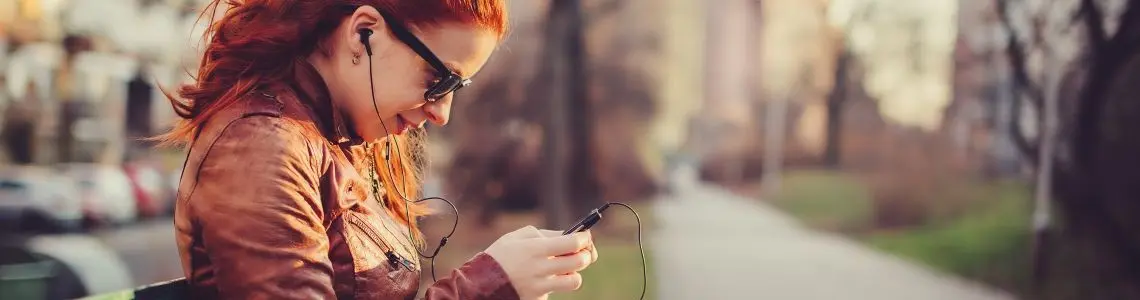 a young woman with curly red hair sitting on a park bench in a park like Central Park accessing her mobile device