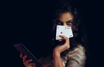 mysterious dark-haired woman playing poker online being devious as she covers her face with a pair of aces