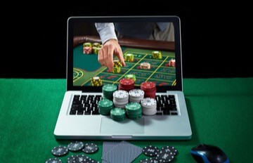 a laptop computer open to an online casino with chips of different colors on the keyboard and around the laptop