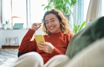 happy young woman curled up on sofa enjoying mobile casino gaming