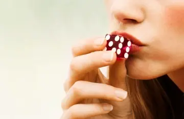 a very pretty woman kissing a red die before rolling the dice in craps