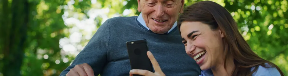 a white haired older man happily spending fun time with his granddaughter as they look at her smartphone