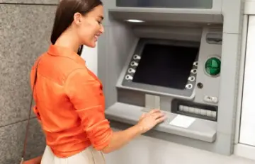 a woman in an orange blouse smiling as she operates an ATM