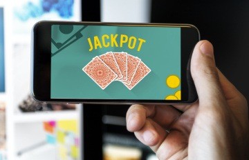 man holding smartphone with jackpot on the screen and five playing cards face down