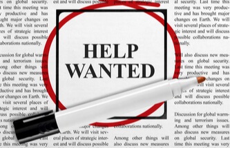 page in the newspaper want ads with the words Help Wanted circled in red with the pen sitting there.