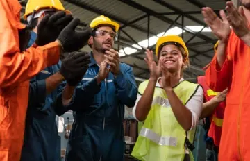 men and women in hard hats at a construction site clapping to celebrate an important achievement