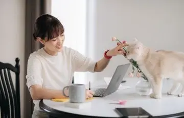 a happy woman celebrating winning at an online casino.  Her cat and a cup of coffee are also on the table.