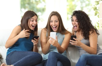three friends on the sofa playing and winning on their phones