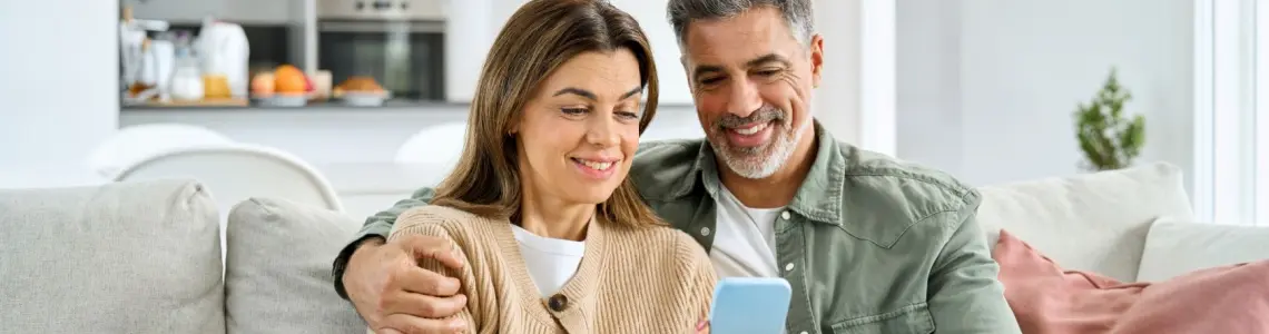a happy, smiling 50-ish couple on the sofa sharing something, possibly a casino game, on their mobile device