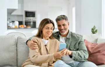 a happy, smiling 50-ish couple on the sofa sharing something, possibly a casino game, on their mobile device