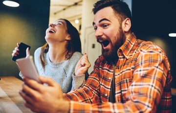 a man and a woman having fun at Everygame Casino on their mobiles