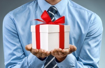 man in blue business shirt with striped tie holding box wrapped with red ribbon