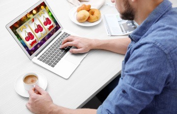 young man with short beard playing slots online with coffee and donuts next to him